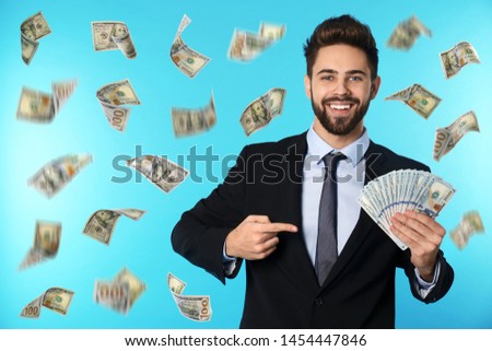 Happy young businessman with dollars under money rain on blue background