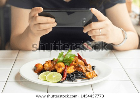 female take food photo with mobile phone spaghetti charcoal seafood on the table in restaurant