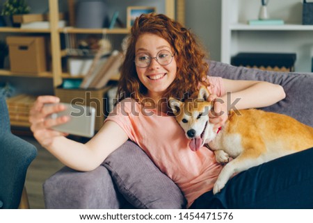 Beautiful girl taking selfie with puppy sitting on couch at home using smartphone camera smiling and posing having fun. People, photographs and animals concept.
