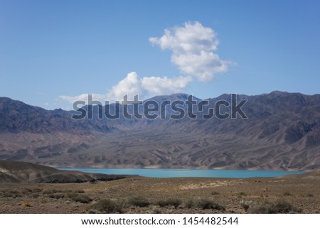Summer mountain landscape with a lake and a white cloud on the blue sky. Lake Bartagoy in Kazakhstan