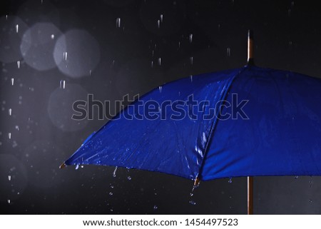 Bright umbrella under rain on dark background