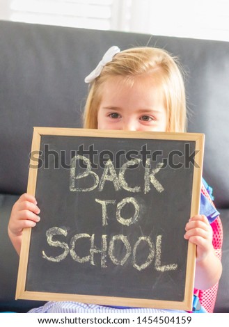 Back to school. A cute blonde little girl showing a chalkboard with "back to school" text