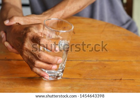 Elderly man is holding his hand while drinking water because Parkinson's disease.Tremor is most symptom and make a trouble for doing activities such as eat or drink.Health care or elderly concept. Royalty-Free Stock Photo #1454643398