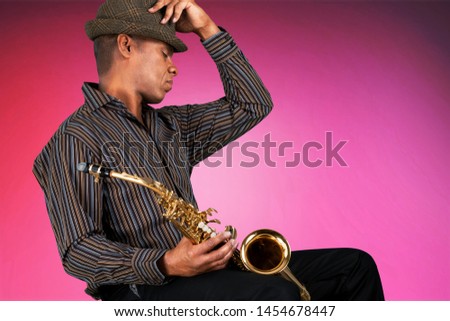 African American handsome jazz musician playing the saxophone in the studio on a neon background. Music concept. Young joyful attractive guy improvising. Close-up retro portrait.
    
    - Image