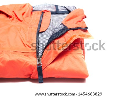 Folded orange zipper windbreaker jacket, rain proof and waterproof hiking Gore-Tex jacket hoodie. Track jacket sport nylon full zip isolated on white. Folded clothes. Outer layer garment for travel.