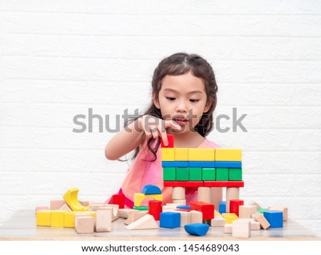Little cute girl 6 years old playing wooden blocks on table and white bricks wall  background. Learning and education. Royalty-Free Stock Photo #1454689043