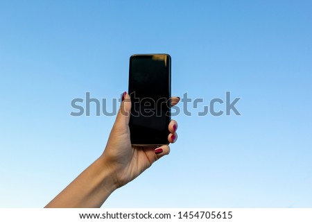 Woman hand with modern smartphone on on blue sky. Blank screen smartphone. Mobile communication network, information concept.