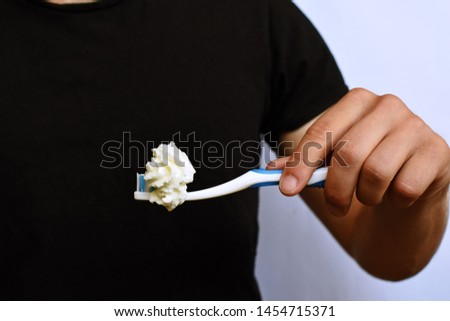 A man holds a toothbrush in front of his torso, instead of toothpaste is cream on the brushes - Abstract concept for dental hygiene and against sugary number-pas