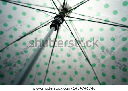 Green and white polka dots umbrella with blurred drops of falling rain under the sunlight. Rainy season, Monsoon coming, Photography during the rainy season theme. (selective focus, space for text)