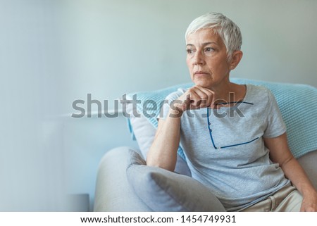 Feeling Down. Middle aged woman in glasses looking down. Portrait of pensive worried senior woman looking through the window and thinking. Pensive woman.  Royalty-Free Stock Photo #1454749931