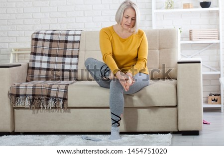 Middle-aged woman suffering from pain in leg at home, closeup. Physical injury concept. Ankle pain, painful point. Royalty-Free Stock Photo #1454751020