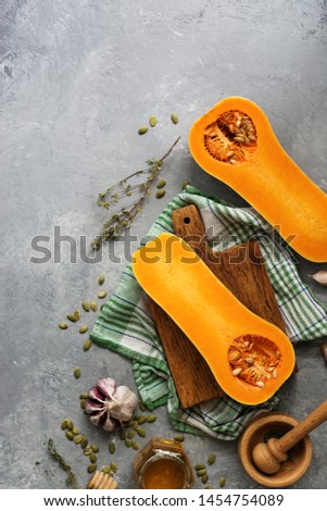 Raw pumpkin halves or butternut squash, cutting board, herbs, honey on a gray background. Top view, flat lay, copy space