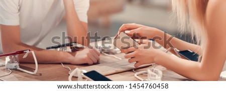 Close up view of young curious man getting instructions for a mobile from professional girl seller in a tech store.