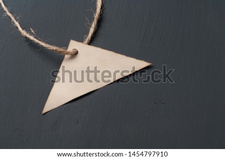 Empty old blank paper price tag in form of triangle with rope lies on dark cement. Business and black friday concept