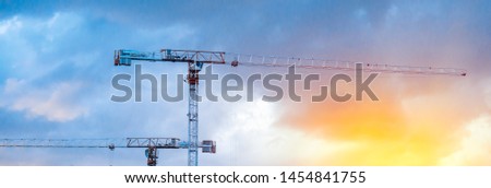 Construction cranes on blue sky with sunset background. Wide banner image.