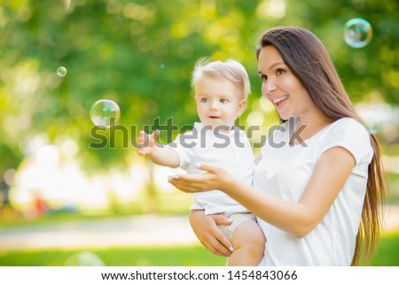 Happy family, Young mother and baby son blowing soap bubbles outdoor park.