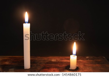 A big and a small candle on a wood surface on a black background