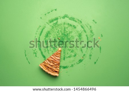 Single last piece of apple pie and the grease traces of the whole pie, on a green paper background. Above view of eaten traditional autumn dessert.