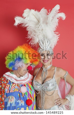 Portrait of happy senior showgirl with sad clown standing against red background