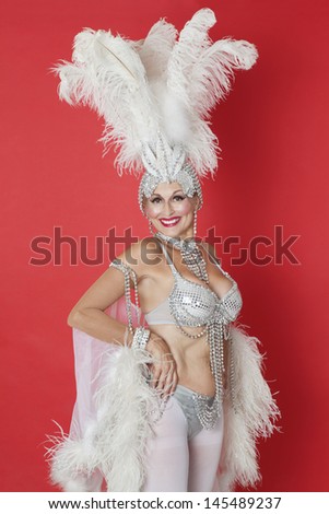 Portrait of senior woman in showgirl's outfit and feather headpiece over red background Royalty-Free Stock Photo #145489237