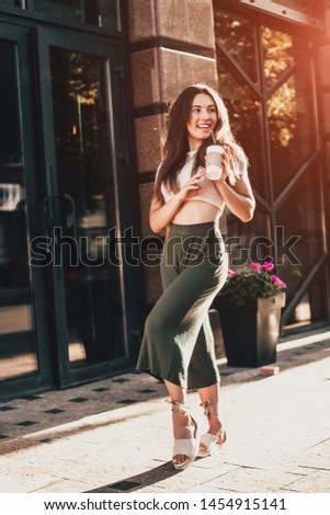 Smiling woman drink coffee walking on the city in summer day.