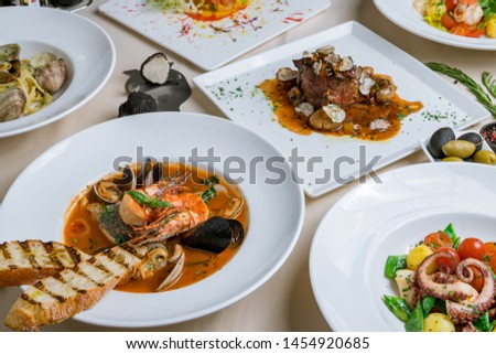 Assorted foodset of European food on table. Seafood casserole bowl, file minion with truffle, vongole, salad with octopus, salad with shrimps