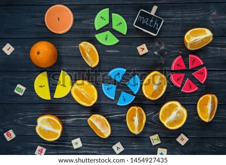 Сolorful math fractions and oranges as a sample on dark wooden background or table. Interesting creative funny math for kids. Education, back to school concept. Geometry and mathematics materials.