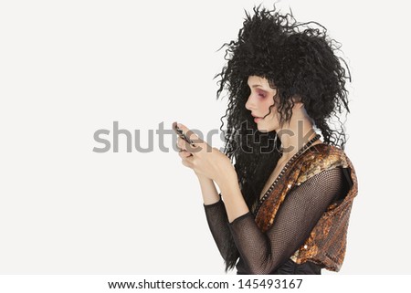 Side view of young Goth woman with teased hair texting on mobile phone over gray background