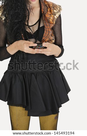 Midsection of young Goth woman text messaging on cell phone over gray background