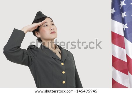 Serious female US military officer saluting American flag over gray background