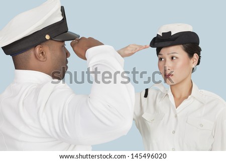 Multi-ethnic US Navy officers saluting each other over light blue background