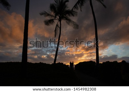 Silhouette of people taking photo of sunset with beautiful clouds in Hawaii at Sunset and palm trees