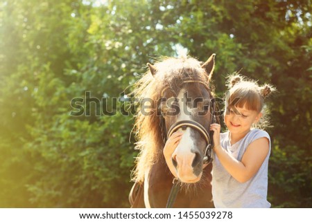 Cute little girl with her pony in park on sunny day 