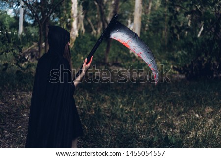 Woman horror ghost holding reaper in forest, halloween concept