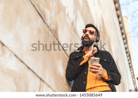Hipster Latin Man Listening Music on Headphones Outdoors - Handsome Latin Guy Feeling the Music in the City - Latin American Guy Using Cell Phone and Listening Music. Lifestyle Concept.