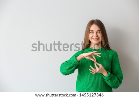 Young deaf mute woman using sign language on light background Royalty-Free Stock Photo #1455127346