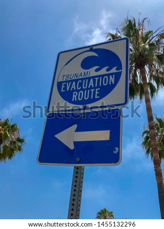 Tsunami evacuation route sign in Venice Beach, California, USA. Evacuation route at danger of a tsunami on a blue sky background with palm trees.