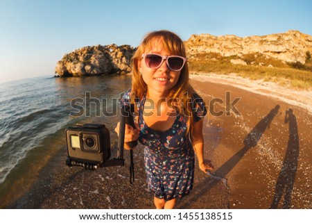 Girl in dress shoots video on action camera on a wild beach.