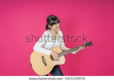 Young asian woman playing acoustic guitar on pink background