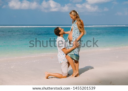 Young pregnant woman with husband expecting baby at tropical beach with blue sea