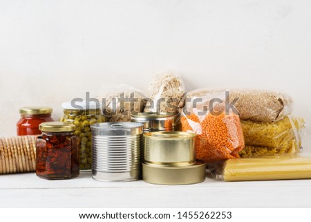 Various canned food and raw cereal grains on a table. Set of grocery goods for cooking, delivery or donation. Copy space. Royalty-Free Stock Photo #1455262253