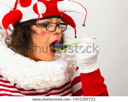 Healthy food for children, concept.Funny joker in red and white clothes is eating fresh blackberry. Close Up portrait on white background.