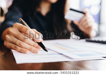 Businesswoman holding pen pointing on summary report chart while holding credit card and using a laptop in the cafe. Technology, ecommerce and online payment concept. Royalty-Free Stock Photo #1455315221