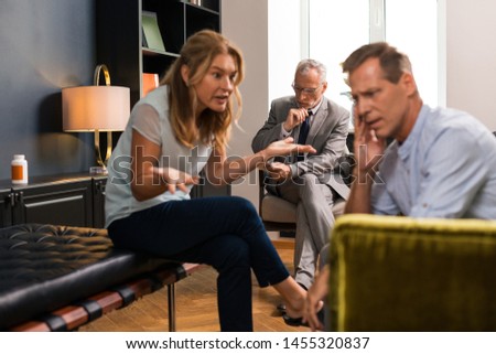 Showing emotions. Bad-tempered middle-aged woman yelling at her upset husband sitting next to her