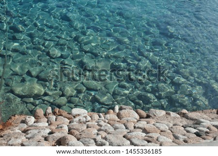 Stone sea bottom.  Part of stones on land, part of stones in azure sea water Royalty-Free Stock Photo #1455336185