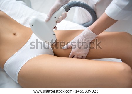 Aesthetic body treatment. Close up top angle portrait of cosmetologist making hair removal procedure of bikini zone to young relaxed woman in white underwear
