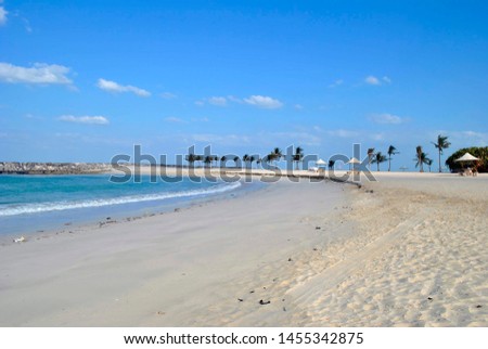 Part of the beach with white sand, a small wave of the ocean, palm trees and umbrellas in the distance Royalty-Free Stock Photo #1455342875