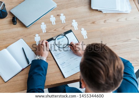 selective focus of man holding magnifier near clipboard with resume 