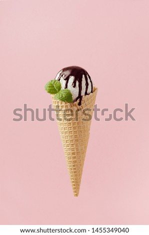 White creamy ice cream in crisp waffle cone with chocolate sauce, fresh green mint leaf on pastel pink background.