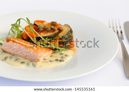 Fish fillet with lemon, vegetables and sauce in white plate.